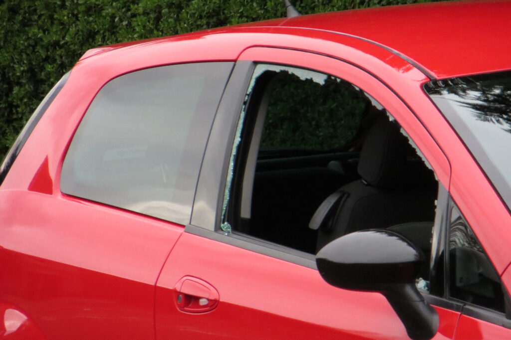 A red car with a broken window in the aftermath of a smash-and-grab crime.